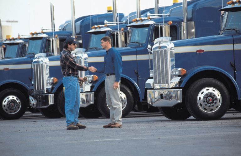 Two Men Shaking Hands in Front of Semi Trucks
