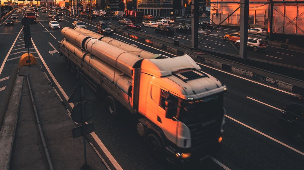 Semi Truck Hauling Pipes on City Freeway at Dusk